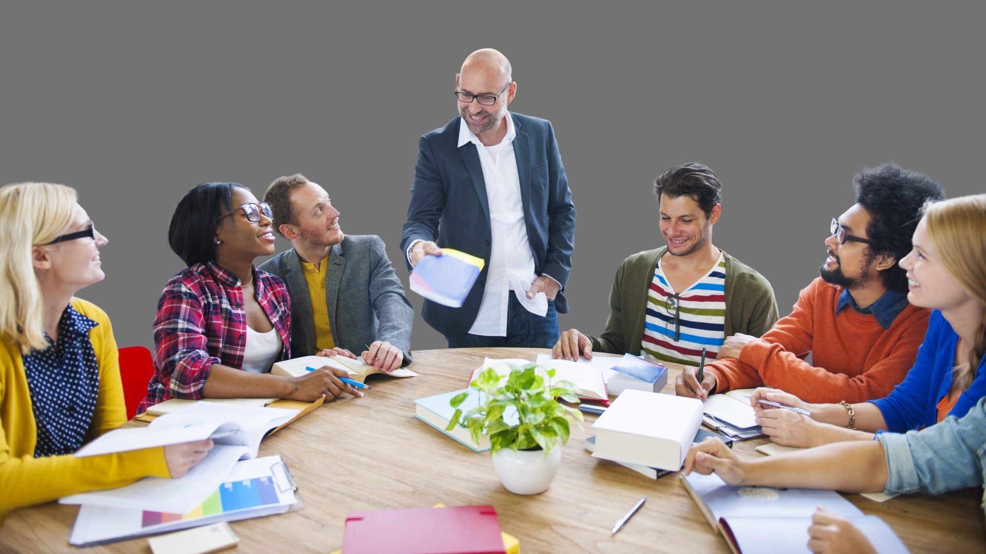 Photograph of adults around a round table, with facilitator standing and talking in center