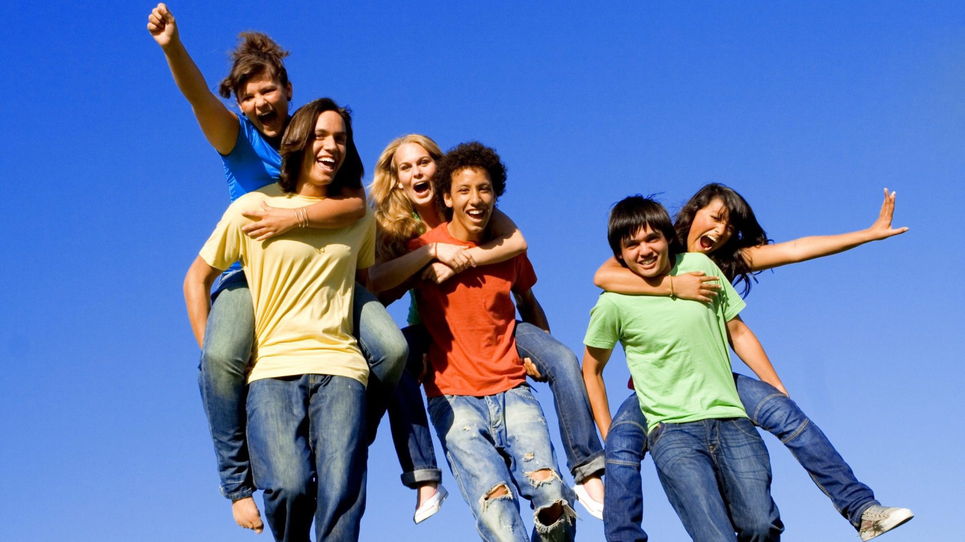 Group of youth running outside, several riding on the backs of others