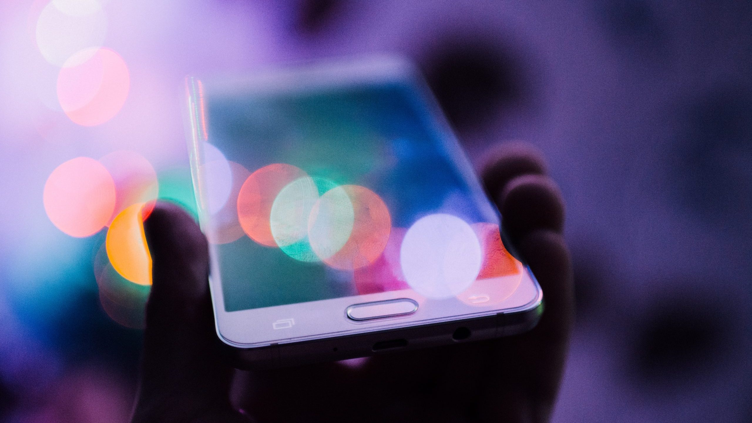 Photograph of hand holding smartphone, with blur of rainbow-like circles of light blurring on top