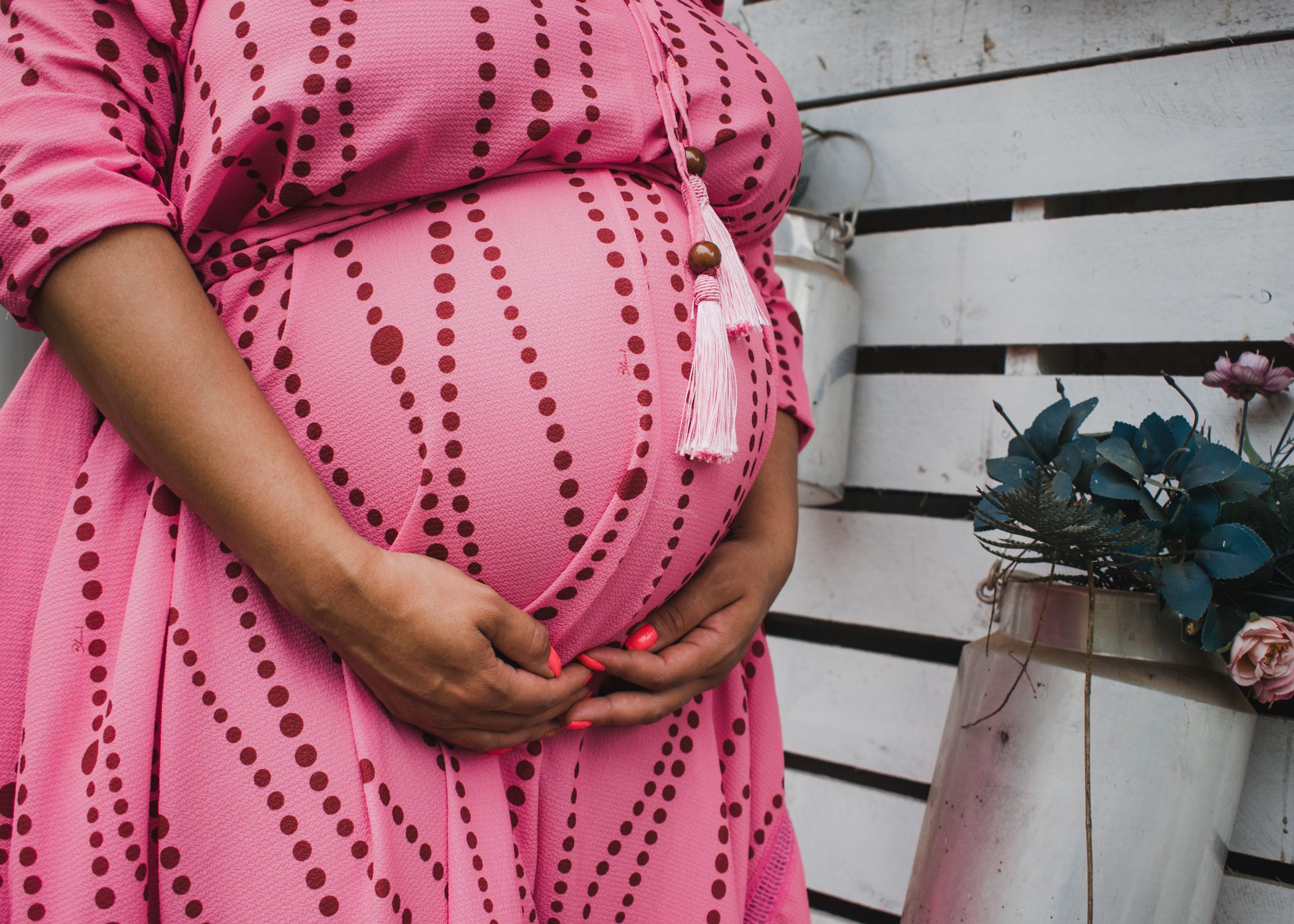 young woman wearing a pink dress with maroon patterned dots, cradling her pregnant belly