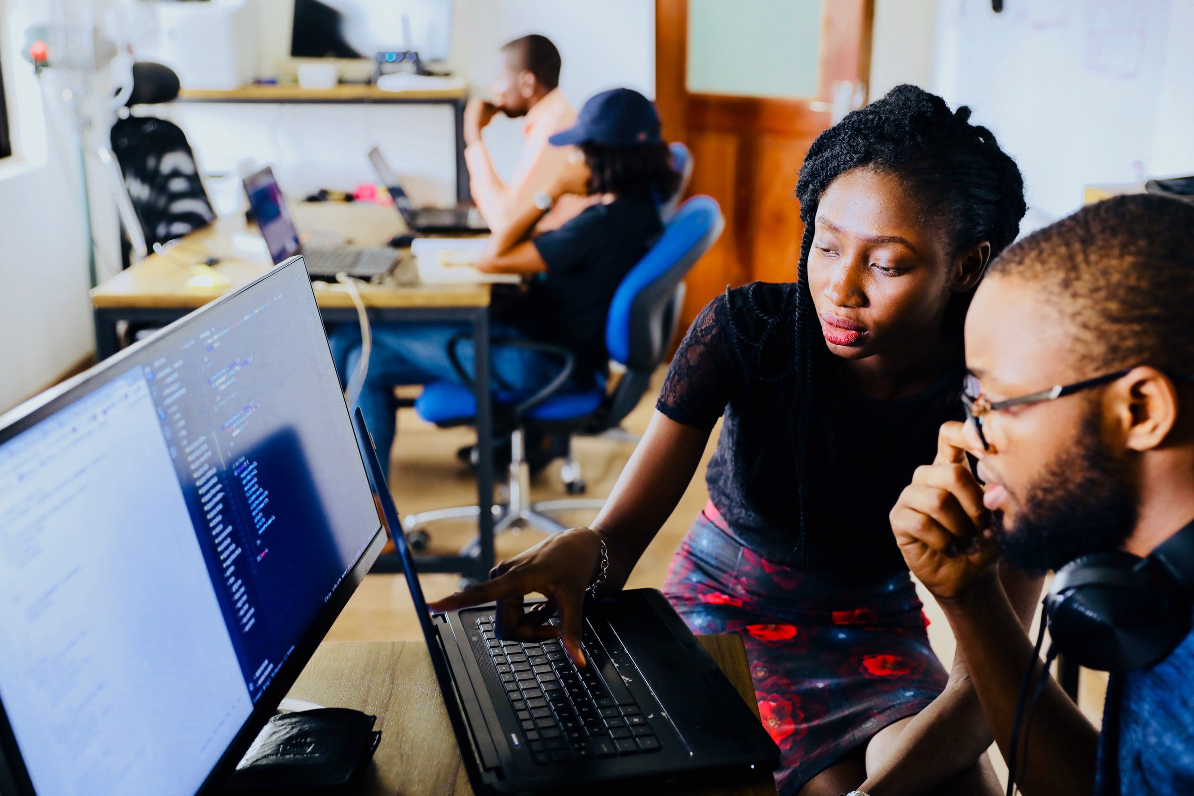 man and woman looking a data on a laptop and comupter monitor