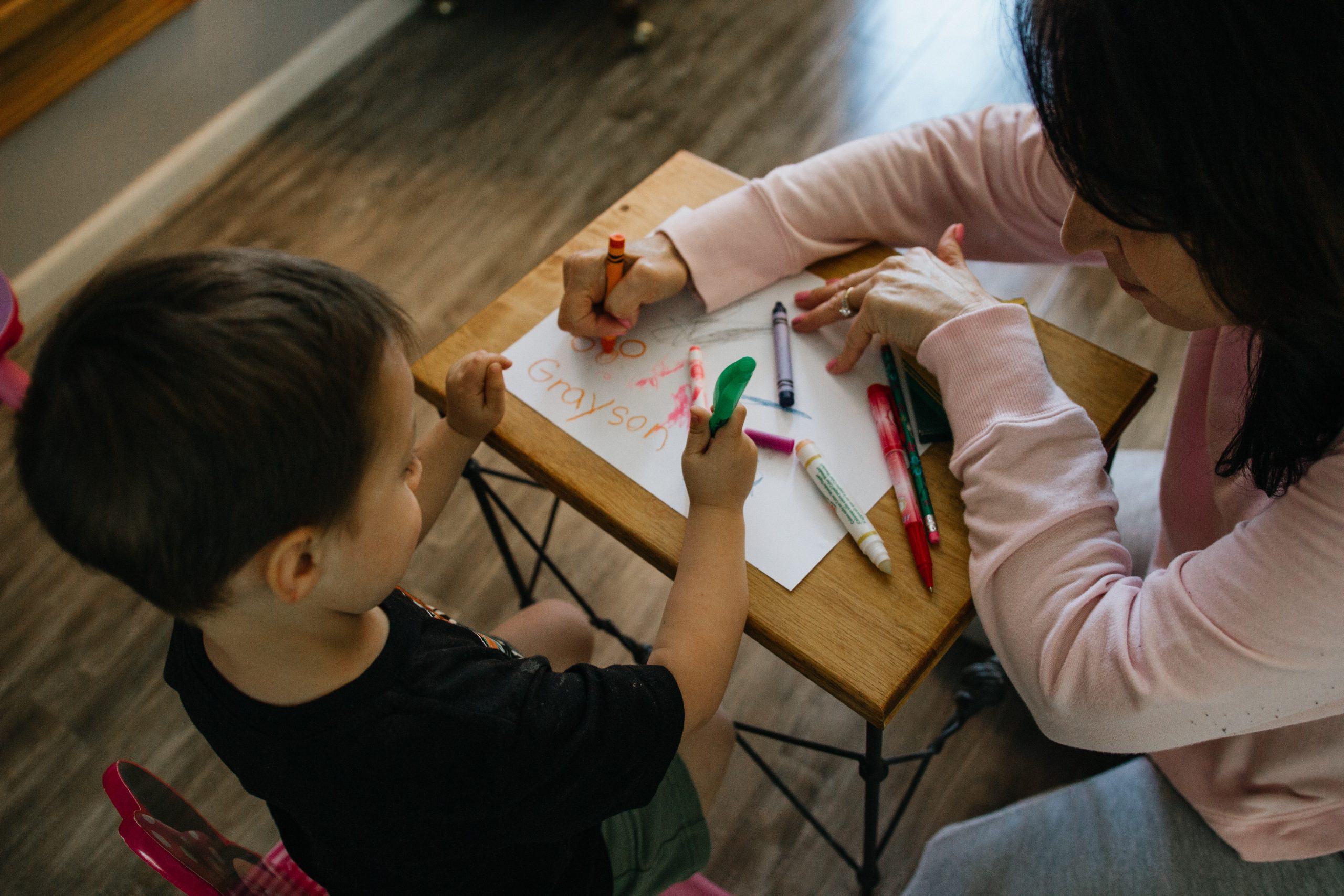 Mom and son sit at desk and color on page