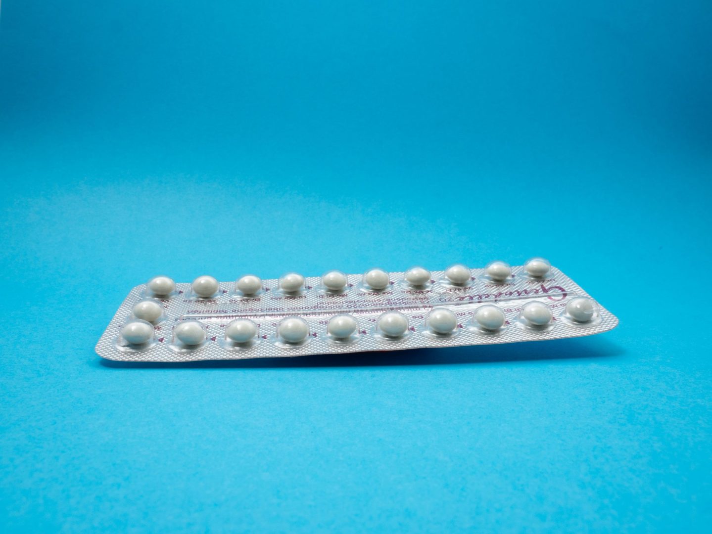 White birth control pill in wrapper on a blue background