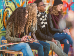 Youth-sitting-on-a-bench-next-to-a-brick-wall-with-colorful-grafiti-300x225