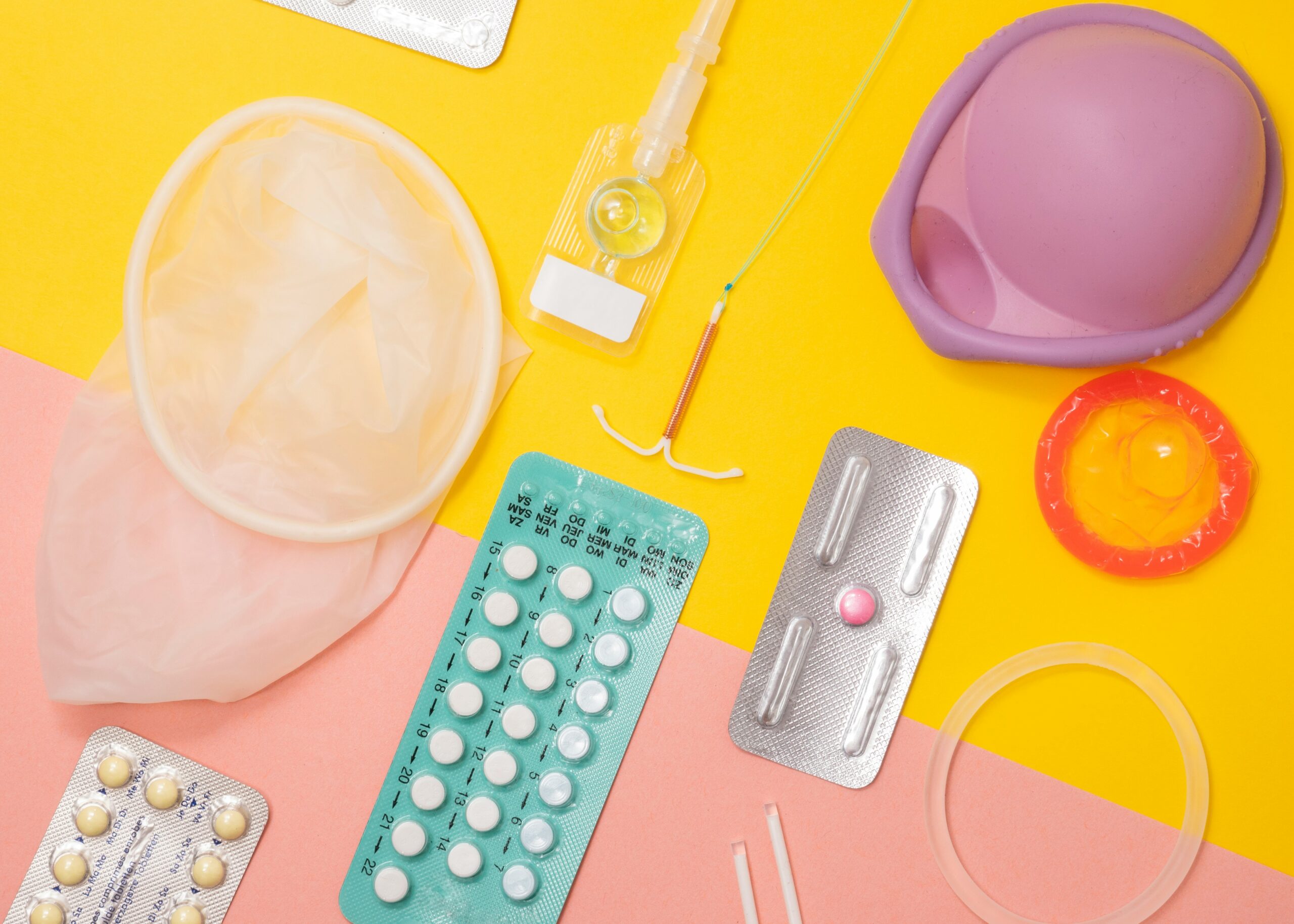 A variety of different contraceptives sitting on a yellow and pink background