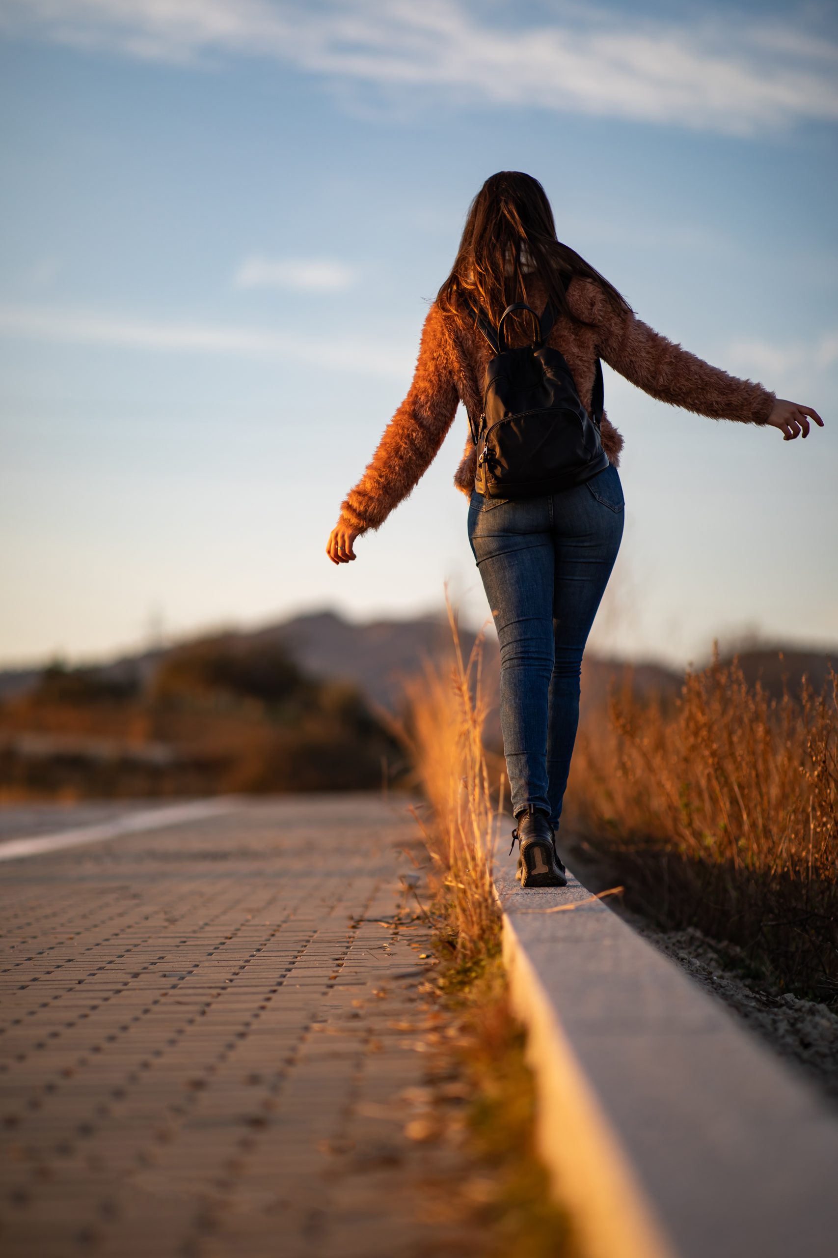woman walking and balancing on street curb or curbstone during sunset